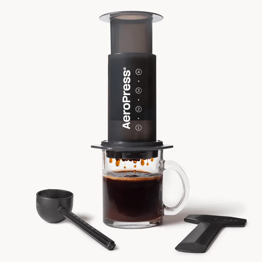 AeroPress Original coffee maker on a mug of brewed coffee, with scoop and stirrer