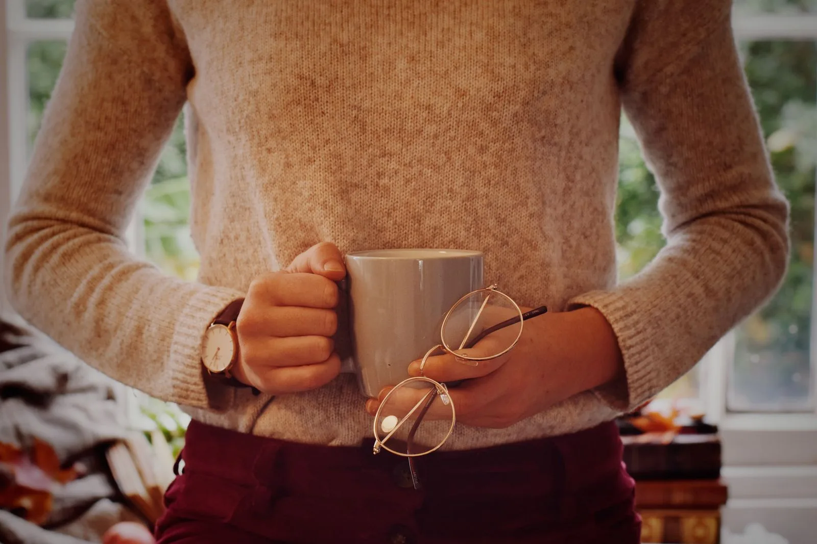 Person seated at a table holding a coffee cup with the other hand resting on their stomach