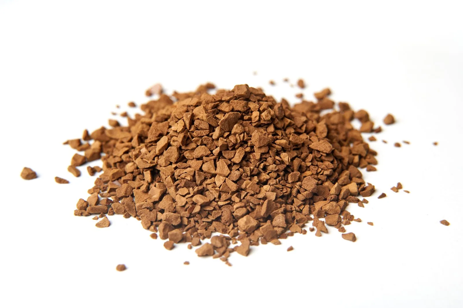 Macro shot of coarse brown coffee granules piled on a clean white background