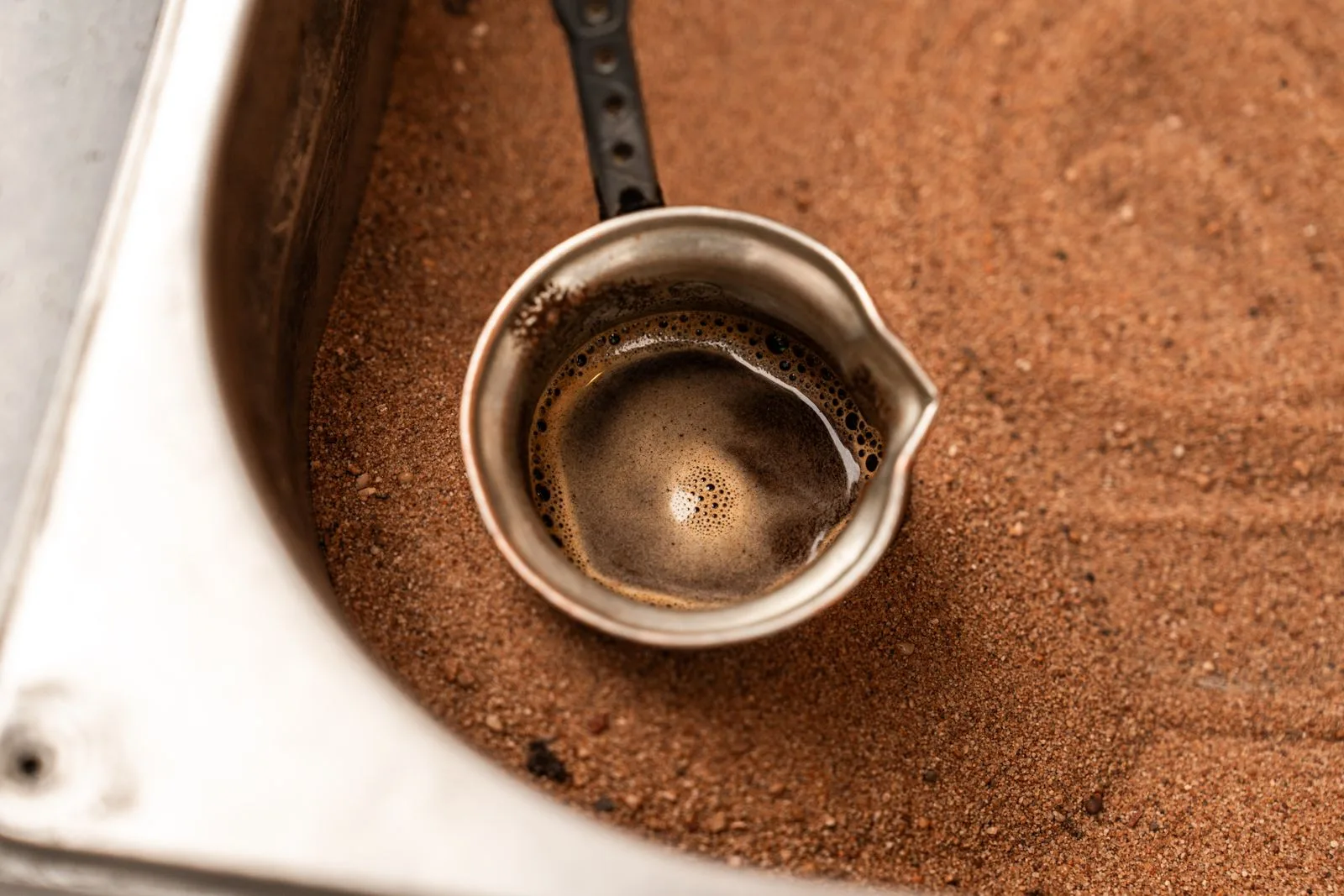 Traditional copper cezve pot simmering over low heat with Turkish coffee foam rising toward the rim