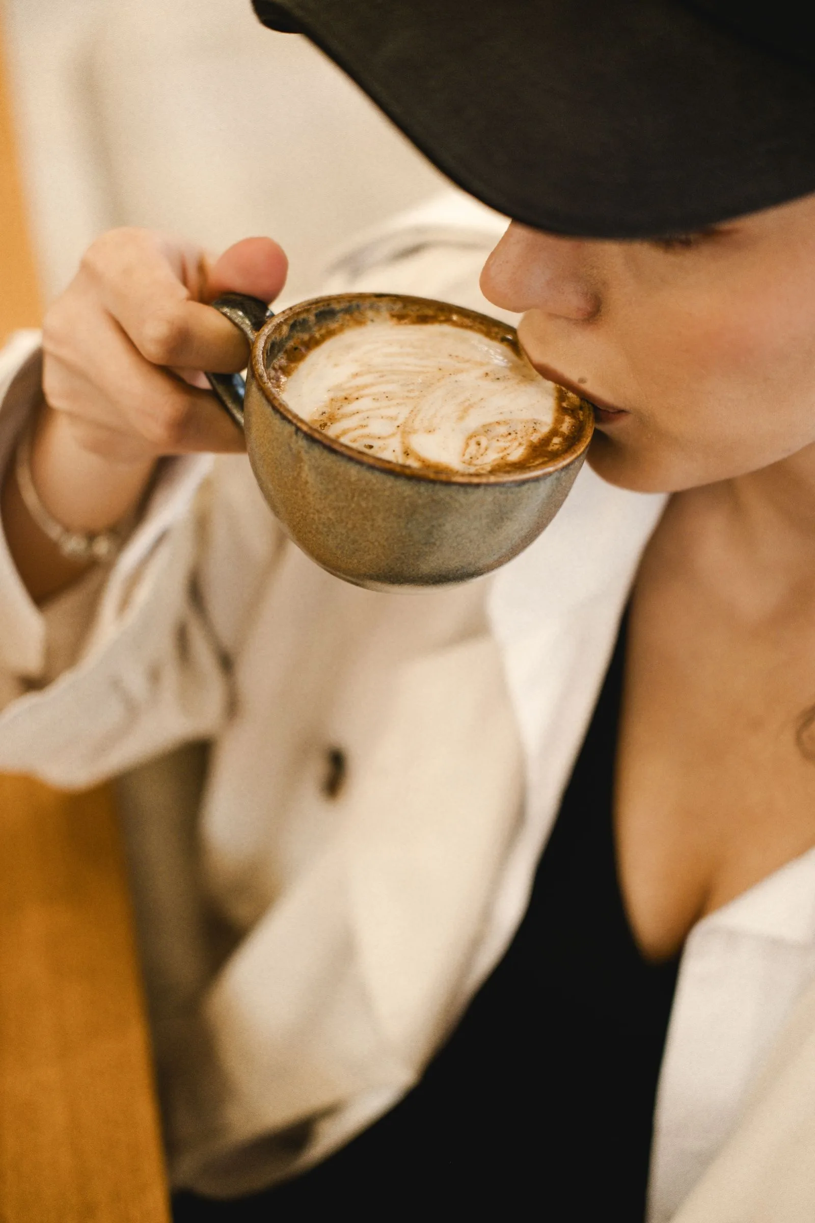 Woman tasting coffee from a white cup, eyes focused on flavor
